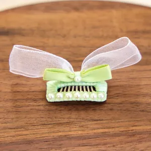 Détail d'une pince à cheveux avec nœud en tissu vert, organza blanc et perles