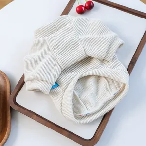 Close-up of cream waffle knit pet sweater texture with small blue side label on a wooden tray