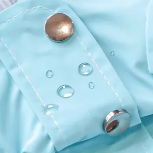 Macro detail of sky blue waterproof fabric with silver snaps and clear water droplets