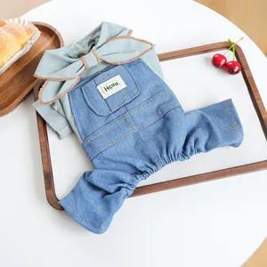 Dog outfit with large green bow shirt and denim overalls on a wooden tray with fruit