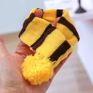 Detail van een mini gebreide geel-bruine gestreepte huisdiersjaal met pompons