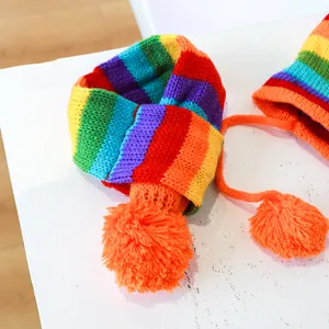 Detail van regenboog gebreide sjaal en muts set met oranje pompons op wit hout