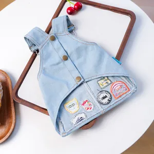 Detail van blauwe denim huisdierjurk met metalen gespen en kleurrijke geborduurde badges