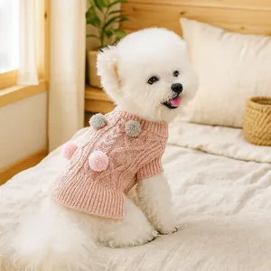 Detailed knit texture and plush pom-poms on a pink dog sweater worn by a Bichon Frise