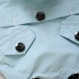 Detail of light blue waterproof dog raincoat showing diagonal weave fabric and metal snaps