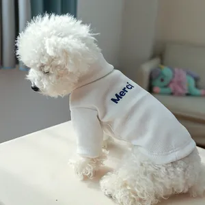 Close-up of cream ribbed pet sweater with blue Merci embroidery on a white Bichon dog
