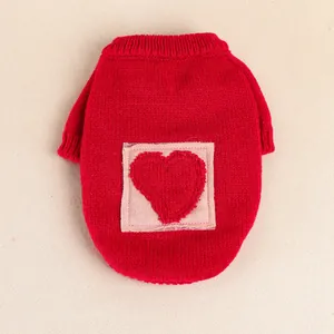 Close-up of red knit pet sweater with pink heart patch and ribbed cuffs on textured fabric