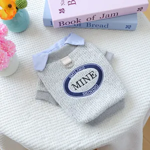 Close-up of grey dog sweater featuring metal D-ring, striped collar and slogan patch