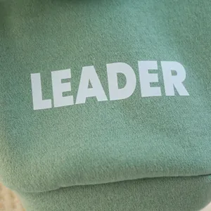 Close-up of soft light green knit fabric featuring white LEADER printed lettering