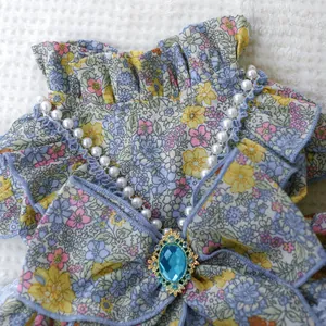 Detail of floral pet dress with ruffles, pearl beads, and a large blue gem accent