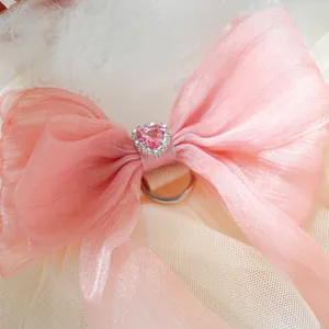 Detailed close-up of pink bow with heart gemstone on lace pet wedding dress