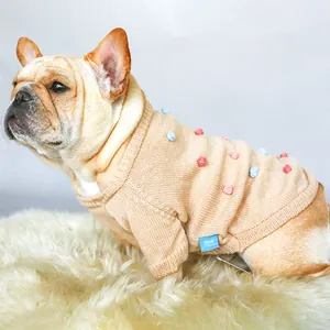 Close-up of beige knit dog sweater with colorful pom-poms and ribbed edges detail
