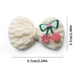 Detailed view of 5.7cm knitted cream bow hair clip with cherry embroidery and gold letters