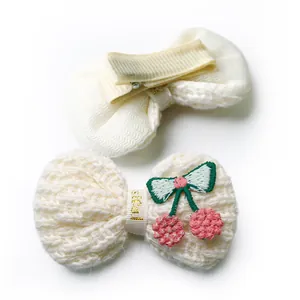 Close-up of knit cream pet hair bow with cherry embroidery and ribbon wrap clip