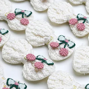 Macro detail of white knit hair bows featuring cherry embroidery and gold text ribbons