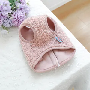 Dettaglio del gilet rosa in pile sherpa per animali su tovaglia di pizzo bianca