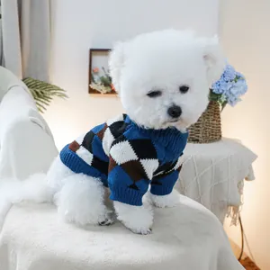 Close-up of a Bichon wearing a blue and brown argyle knit pet sweater in a cozy setting