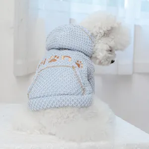 Macro shot of light blue waffle-knit pet hoodie with orange paw embroidery on small dog