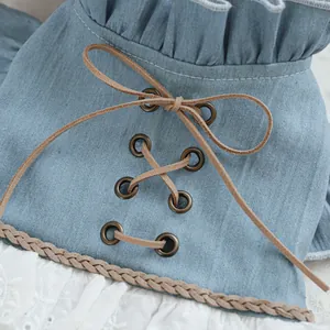 Detailed close-up of blue denim pet dress with brown lacing and white lace trim