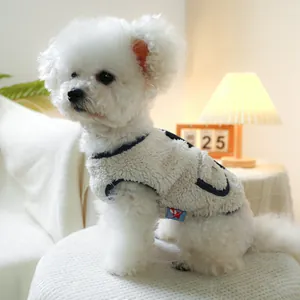 Close-up of plush white pet vest with navy trim and brand tag on a Bichon Frise dog