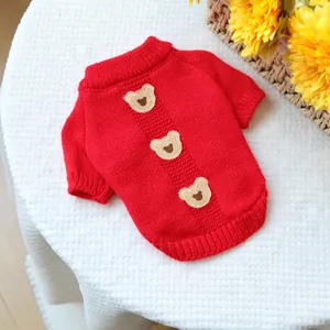 Detail of red pet sweater with three teddy bear patches and knit ribbing on white fabric
