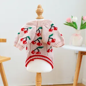 Detailed knit texture of a pink pet sweater featuring red cherry patterns on a model