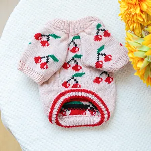 Detail of pink knitted pet sweater with cherry pattern on white plush background