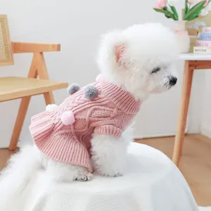Detailed knit texture of pink pet sweater with colorful pom-poms on cable knit fabric