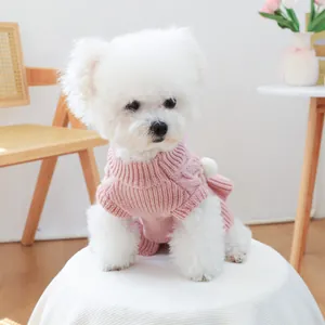 Detailed knit texture and pom-pom detail on a pink dog sweater worn by a Bichon Frise