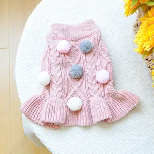 Detail of pink knitted dog dress with colorful pom-poms and ruffled hemline texture