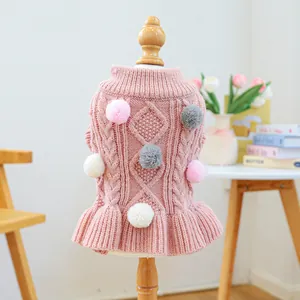 Detail of pink knitted pet sweater with cable knit texture, pom-poms, and ruffled hem