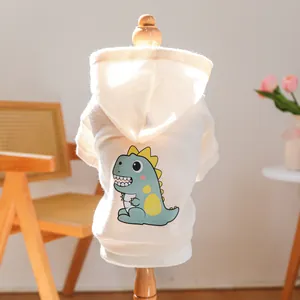 Detail view of cream pet hoodie with cartoon dinosaur print on a wooden hanger