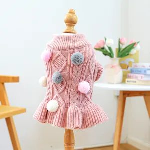 Detail of pink knit dog sweater with cable pattern, colorful pom-poms and ruffled hem detail