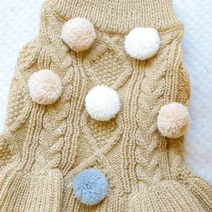 Macro detail of khaki cable knit pet sweater with colorful plush pom-poms and ribbed collar