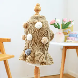 Close-up of khaki knit pet dress with pom-poms and ruffled hem on a wooden mannequin