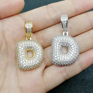 Dettaglio di ciondoli a lettera D in oro e argento con zirconi tenuti in mano