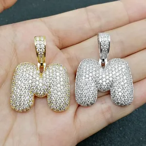 Dettaglio dei ciondoli a lettera M a bolla in oro e argento con micro-pave di zirconi