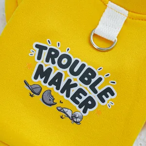 Detail eines gelben Hundegeschirrs mit Trouble Maker Aufdruck und Metall D-Ring