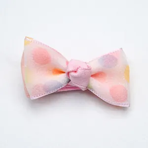 Detailed view of a pink polka dot bow hair clip for pets with soft fabric texture