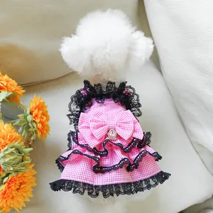 Detailed view of pink plaid dog dress with black lace trim and bow on white poodle