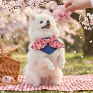Blue denim pet neckerchief with red gingham bow against a spring cherry blossom background