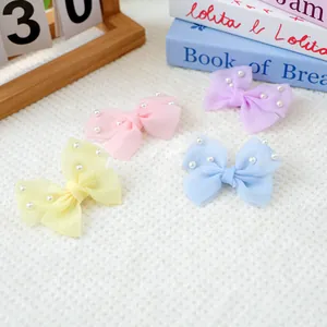 Détail de quatre barrettes nœuds en tulle colorés avec perles sur un tapis blanc doux