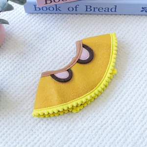 Detailed view of yellow felt pet bandana with cartoon eyes and soft pom-pom trim detail