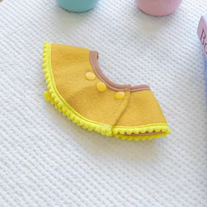 Detail view of ginger yellow pet bandana with plush pom-poms and three yellow buttons