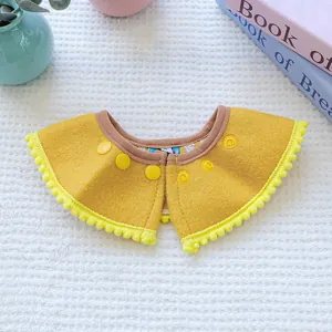 Ginger yellow pet bib with pom-pom trim and snap buttons on a waffle fabric background