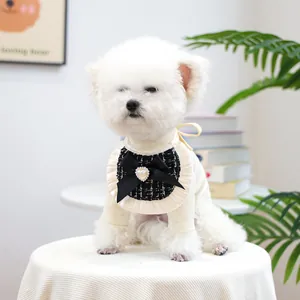 Close-up of cream knit dog sweater with tweed bib, black bow, and heart pearl detail