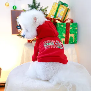 Rear view of a small white dog in a red Christmas pet hoodie with a holiday cookie pattern