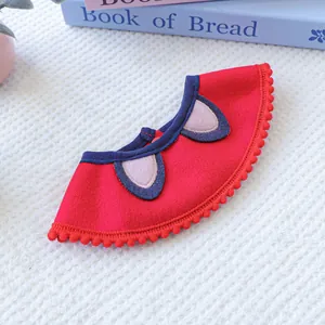 Detail of red pet bib with pink round ears and pom-pom trim on white texture background