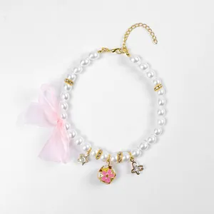 Gros plan d'un collier de perles pour animaux avec nœud en organza rose et charms