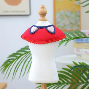 Detail of red pet bib with pom-pom trim and blue-pink ear accents on white mannequin